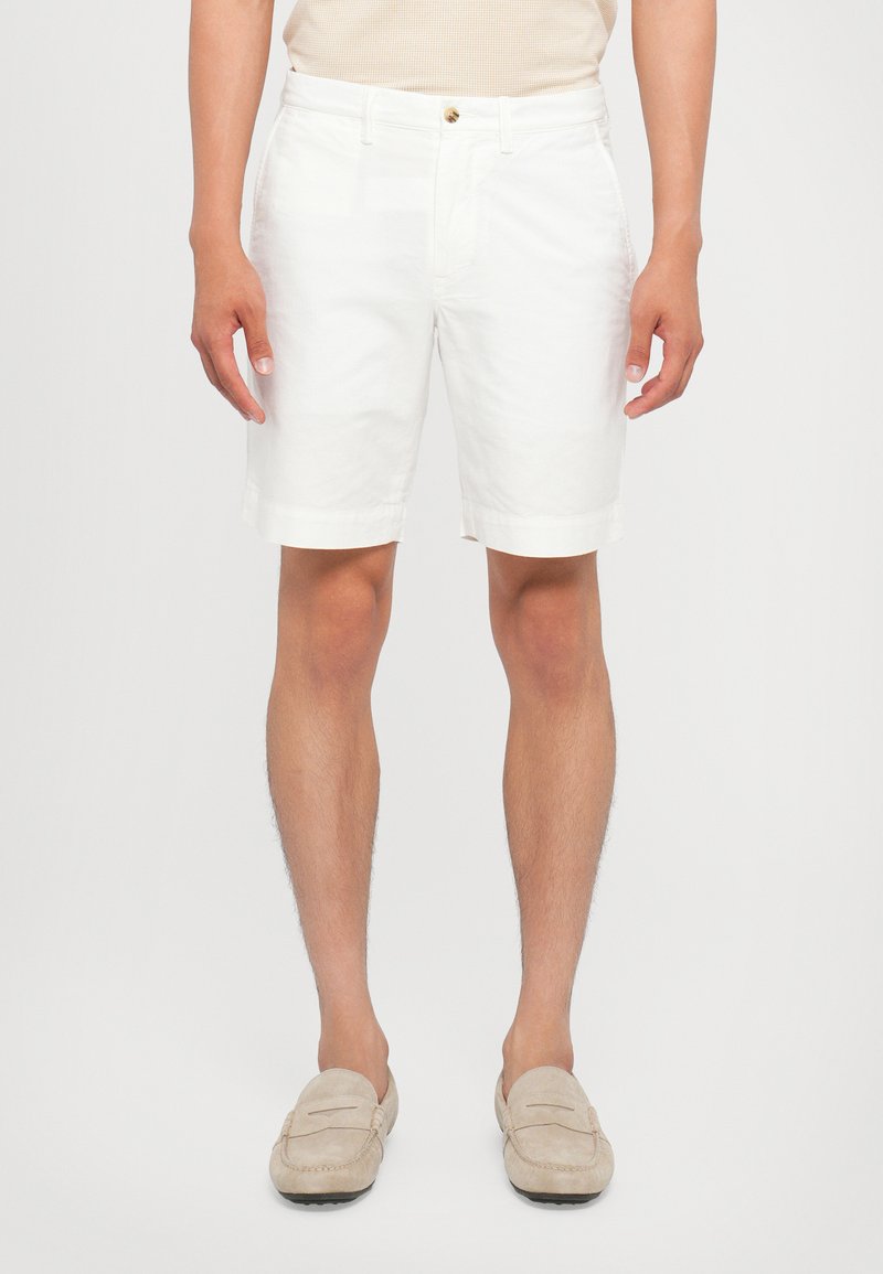 Hvite bomullshorts med en slim fit, midt på låret lengde og rullet kant. Har gull knappelukking og sidelommer.