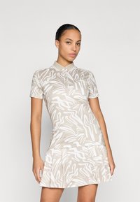 Přiléhavé béžové polo šaty s bílými abstraktními vzory, krátké rukávy a skládací sukně. Mají klasický límeček a knoflíkovou légou.