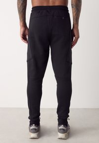 Zwarte joggerbroek met een aansluitend ontwerp, elastische tailleband, zijzakken en een gestructureerde stof. Gecombineerd met atletische schoenen in neutrale tinten.