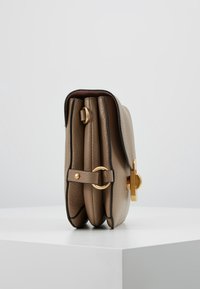 Bolso de cuero beige con un diseño estructurado, que presenta un cierre con tono dorado, herrajes decorativos y una textura suave.