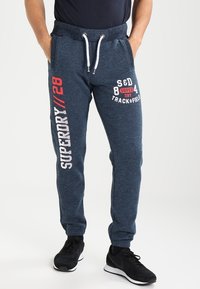 Marineblauwe sweatpants met een zachte textuur, voorzien van witte en rode bedrukte tekst op het linkerbeen en een drawstring tailleband.