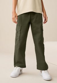 Olívovo zelené nákladné nohavice z mäkkej látky, vybavené bočnými vreckami, voľným strihom a rovnými nohavicami. Kombinované s bielymi teniskami.