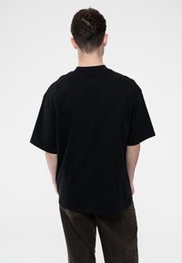 Black cotton t-shirt with a relaxed fit, short sleeves, and a crew neck; worn with dark brown pants; no visible patterns or logos.