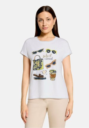 Vrouw met lang bruin haar die een wit T-shirt draagt met zonnebril, een patroon tas, sandalen, een koffiekopje en de tekst "take it casual."