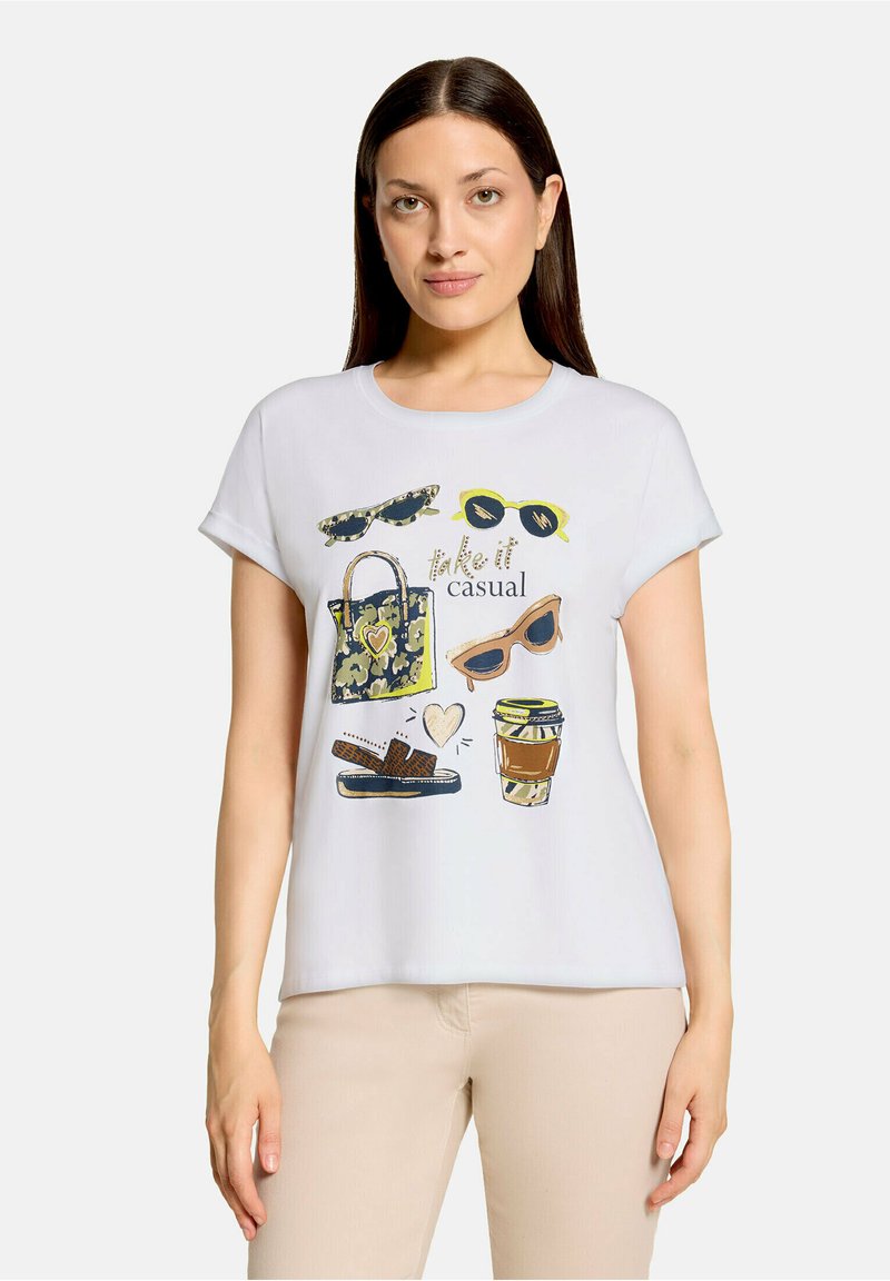 Femme aux longs cheveux bruns portant un t-shirt blanc avec des lunettes de soleil, un sac à motifs, des sandales, une tasse de café, et le texte "take it casual."