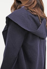 Marineblå hættejakke med et blødt, tekstureret stof. Har en bred krave, en skræddersyet pasform og et diskret design for et elegant udseende.