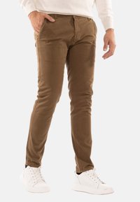Pantaloni slimm fit marroni con una texture liscia, caratterizzati da un classico design a cinque tasche. Indossati con sneakers bianche e un maglione leggero.
