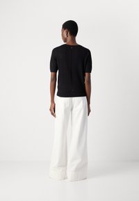 Black short-sleeve knit top with a back fastening and textured detailing, paired with wide-leg white trousers featuring folded cuffs.