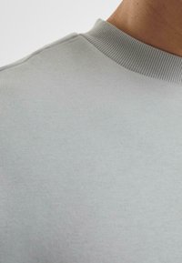 Hellgraues Sweatshirt mit einem gerippten Kragen und glatter Textur, das einen Rundhalsausschnitt aufweist und eine Nahaufnahme des Stoffes zeigt.