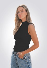 Top nero senza maniche con collo alto, parti arricciate; abbinato a jeans leggeri a vita alta blu chiaro. Modella indossa un bracciale d'oro.