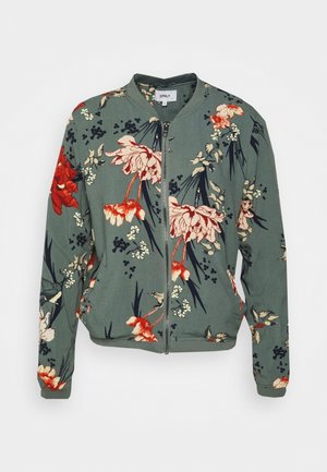 Bloemenprint bomberjack van groene stof. Voorzien van grote rode en roze bloemen met groene bladeren. Heeft een ritssluiting over de hele lengte en geribbelde manchetten.