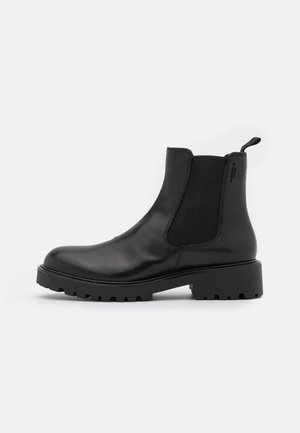 Bottines Chelsea en cuir noir avec des panneaux élastiques sur les côtés et une languette, dotées d'une semelle en caoutchouc épaisse et nervurée. Texture lisse, design épuré.