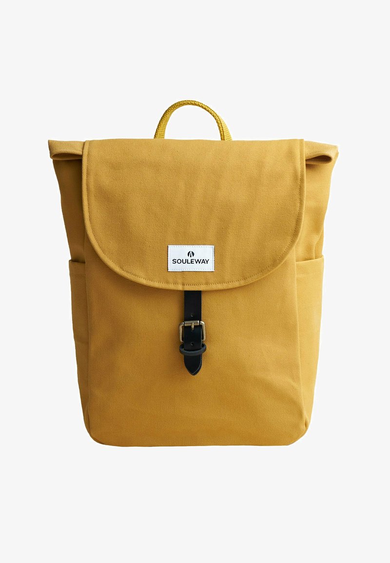 Mochila de lona amarilla con solapa plegable, cierre de hebilla de cuero, bolsillo frontal y un asa en la parte superior. Presenta una etiqueta de la marca en el frente.