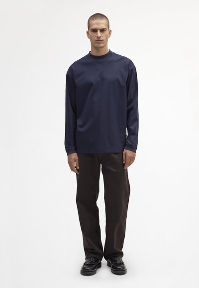 Granatowa koszula z długim rękawem i okrągłym dekoltem, zestawiona z ciemnymi brązowymi spodniami i czarnymi butami. Koszula wykonana jest z gładkiego, elastycznego materiału.