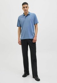 Šviesiai mėlyna polo marškinėliai su trumpomis rankovėmis ir apykakle, derinami su juodomis kelnėmis ir juodais batais, prieš baltą foną.