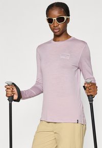 Μακρυμάνικη μπλούζα ανοιχτού μωβ χρώματος με στρογγυλή λαιμόκοψη, που διαθέτει ένα μικρό λογότυπο στο στήθος. Το μοντέλο κρατάει μπαστούνια πεζοπορίας, φοράει μπεζ παντελόνια.