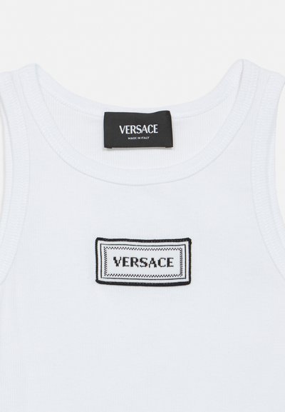Haut blanc sans manches avec étiquette Versace noire cousue à l'avant et étiquette Versace noire fixée à l'intérieur de l'encolure.