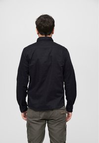 Black long-sleeve shirt with a fitted design and buttoned cuffs, paired with olive cargo pants featuring multiple pockets.