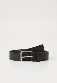 Cinturón de cuero negro con hebilla rectangular plateada que presenta un pequeño detalle de rayas rojas y blancas, enrollado sobre una superficie blanca.