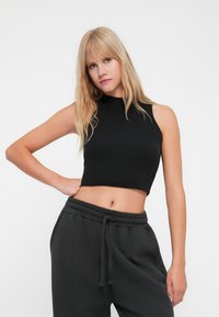 Top court noir, en ribbed, sans manches avec un col haut, associé à un pantalon de survêtement gris foncé confortable avec une taille élastique et un cordon de serrage.