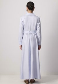 Robe bleu clair à manches longues avec un col, taille cintrée et jupe ample. Tissu lisse avec des poignets boutonnés et une ceinture nouée au dos.