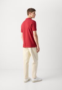 Rotes Polo-Shirt mit Kragen, kombiniert mit cremefarbigen Hosen und weißen Sneakers. Kurze Ärmel, schlichtes Design und keine sichtbaren Muster.