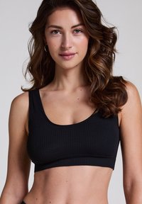 Black ribbed bralette with a scooped neckline and wide straps. Fabric texture is soft and stretchy, offering a comfortable fit.