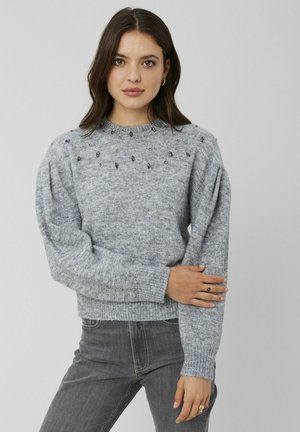 Chandail en tricot gris avec un ourlet et des poignets côtelés, orné de perles décoratives le long des épaules. Texture douce, coupe décontractée et design à col rond.