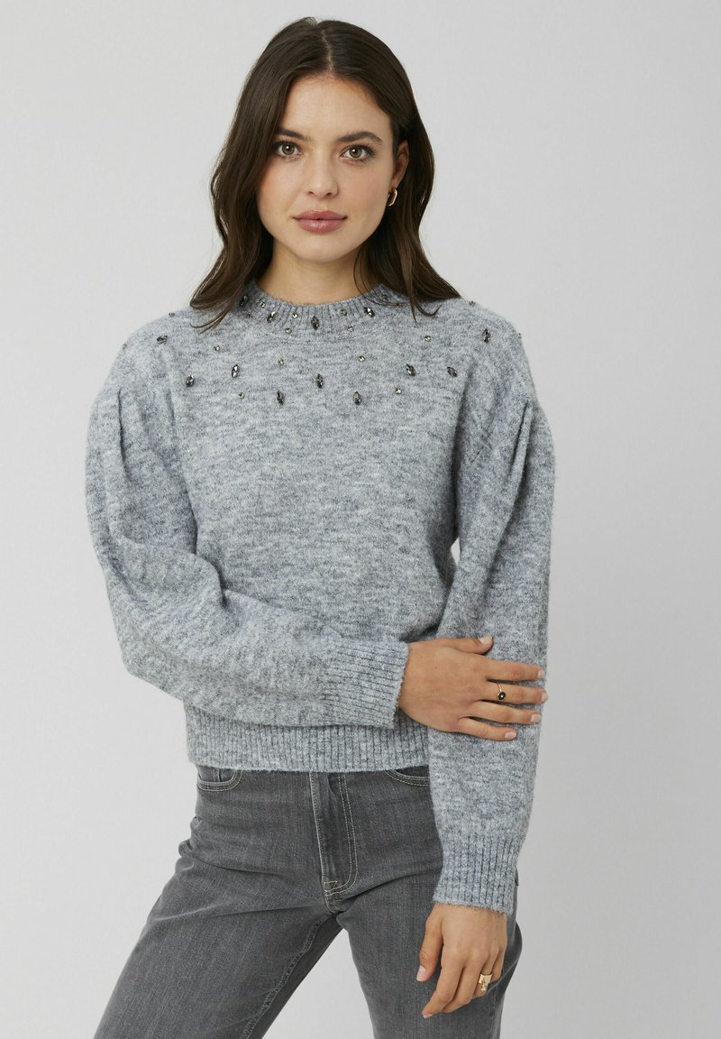 Chandail en tricot gris avec un ourlet et des poignets côtelés, orné de perles décoratives le long des épaules. Texture douce, coupe décontractée et design à col rond.