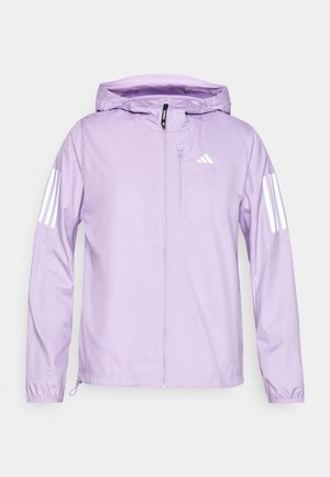 Chaqueta ligera de color púrpura claro con capucha, cuenta con acentos de tres rayas blancas en las mangas y un bolsillo con cremallera en la parte delantera. Textura suave.