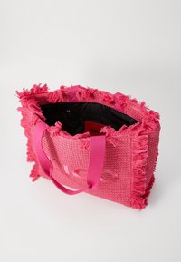 Roze geweven draagtas met rafelige randen, stoffen handvatten en een zwarte binnenkant. Voorzien van een reliëflogo aan de voorkant. Binnenin een zak met rits.