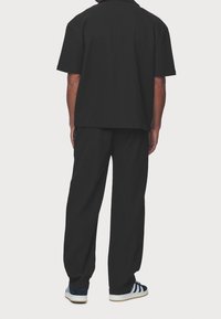 Svart kortärmad skjorta med lös passform, kombinerad med svarta vida byxor och blå-svarta sneakers med vita ränder. Texturerat tyg.