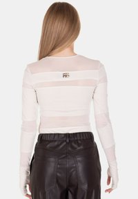 Top a maniche lunghe in tessuto leggero trasparente beige chiaro con righe orizzontali e piccolo logo sul retro, abbinato a pantaloni in ecopelle neri.