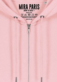 Felpa rosa con zip e coulisse di colore argento, con l'etichetta "MIRA PARIS Born to Rock", realizzata in cotone biologico con istruzioni per il lavaggio stampate all'interno.