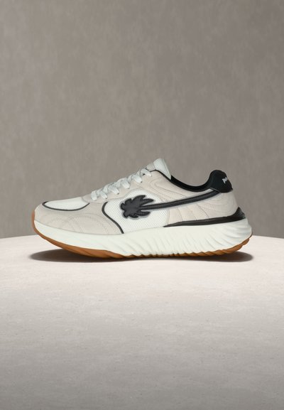 Λευκό αθλητικό παπούτσι με μαύρες λεπτομέρειες, υφασμένο πέλμα και μαύρο λογότυπο σε σχήμα φύλλου στο πλάι, εμφανίζεται σε ουδέτερη επιφάνεια και φόντο.