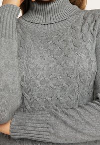 Pull à col roulé en maille grise avec des poignets et un col côtelés, doté d'un motif texturé sur l'ensemble du corps pour plus de chaleur et de confort.