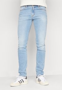 Ljust blå denim skinny jeans med midja i medelhöjd, subtil blekning, fem fickor och kontrasterande sömmar, tillsammans med vita och svarta sneakers.