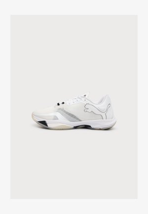 Zapatilla deportiva blanca con detalles en negro y beige, diseño con cordones y un gran logo plateado de Puma en el lateral, mostrada sobre un fondo liso.