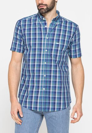 Uomo che indossa una camicia aderente a maniche corte a quadri blu, verde e bianco con colletto e jeans azzurri.
