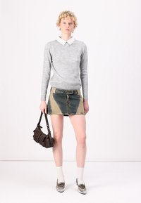 Pulover gri tricotat cu o cămașă albă cu guler dedesubt, asociat cu o fustă din denim în culori contrastante și o geantă de umăr maro. Sosete albe și pantofi argintii.