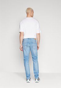 Vaqueros de mezclilla azul claro con un corte recto, cinco bolsillos, etiqueta de cuero en la cinturilla, combinados con una camiseta blanca y zapatillas.