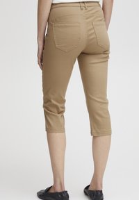 Khaki capri kalhoty s těsným střihem, vyrobené z měkké, pružné látky. Mají dvě zadní kapsy a středně vysoký pas.