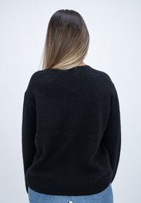 Schwarzer gestrickter Pullover mit lockerer Passform und rundem Halsausschnitt, mit strukturiertem Oberflächenmuster und langen Ärmeln, kombiniert mit hellblauen Jeans.