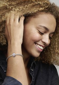 Silberarmband mit geflochtenem Design und lila Edelsteinakzenten. Am Handgelenk getragen, zeigt es eine Hand mit lockigem Haar.