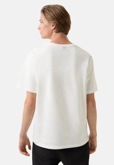 Bílý bavlněný trik s krátkým rukávem, kulatým výstřihem a volným střihem. Hladká textura, minimální značení na lemu a žádné viditelné vzory.