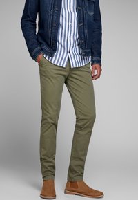 Oliwkowe chinosy o slim fit, w połączeniu z granatową dżinsową kurtką oraz niebieską koszulą w paski z guzikami, a do tego brązowe zamszowe botki Chelsea.