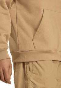 Beige sweatshirt met een kangaroovak, geribbelde boorden en een zachte stoftextuur, gecombineerd met bijpassende lichte broek.
