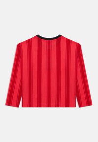 Κόκκινο μακρυμάνικο τοπ με υφή από δίχτυ, με κάθετες ρίγες και μαύρη λαιμόκοψη τύπου crew. Ευθεία τελείωμα, άνετη εφαρμογή.