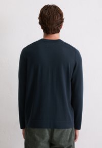 Pull à col rond bleu marine avec des manches longues, col côtelé et ourlet inférieur. Texture lisse et design ajusté, associé à un pantalon vert texturé.