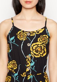 Černé bezramínkové šaty s žlutými a modrými květinovými vzory, s knoflíkovým zapínáním vpředu a nařaseným pasem. Vyrobené z lehké tkaniny.
